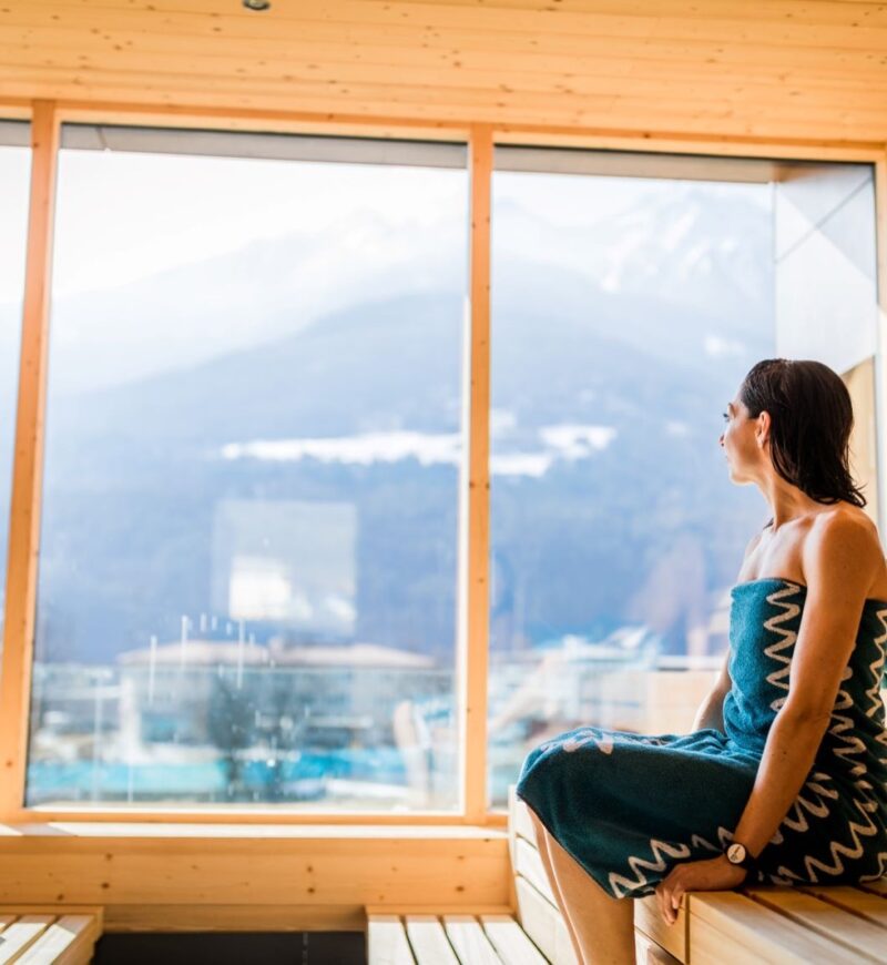 Frau blickt aus der Panorama-Sauna auf die Berge