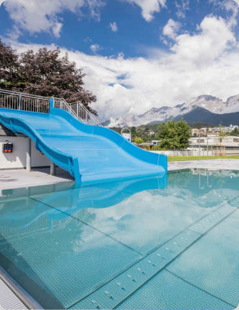 Blaue Wasserrutsche im Freibad vor Bergkulisse