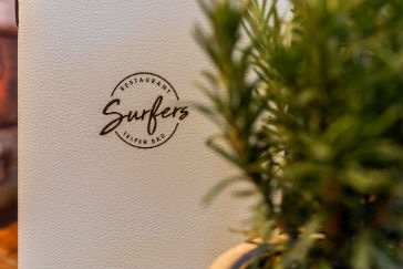 Surfers-Logo an einer hellen Wand mit Pflanze